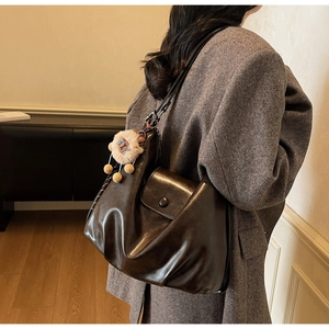 Close-up of dark brown leather tote bag featuring a pleated design and a cute lion plush charm