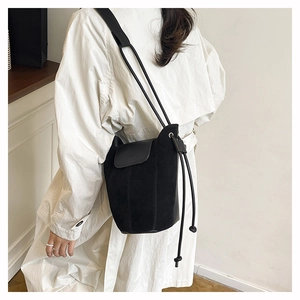 Close-up of black matte suede bucket bag with leather flap and drawstring closure details