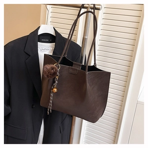 Detail of a dark brown faux leather tote bag with brand embossing and plush charm