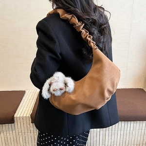 Detail of caramel brown dumpling bag featuring pleated shoulder strap and plush rabbit charm