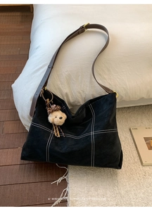 Detail of black tote bag featuring white stitching with a plush bear charm on a bed