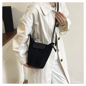 Detail of matte suede bucket bag with leather flap worn with a minimalist white coat