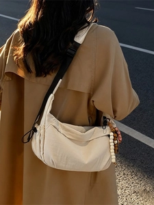 Minimalist cream nylon crescent shoulder bag featuring black drawstring and tassel details