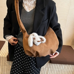 Brown faux suede crescent bag detail with white plush bunny charm on shoulder strap