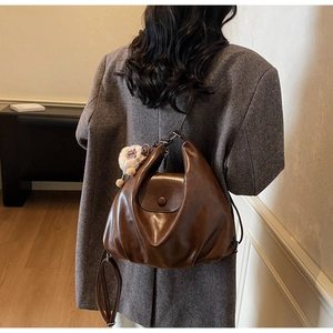 Detail of a brown leather crossbody bag with pleated design and soft pompom charm