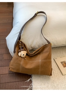 Brown suede hobo bag with white cross-stitching and a cute plush bear pendant accessory