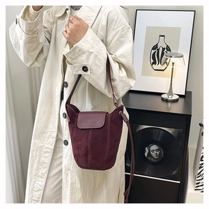 Detail of burgundy suede bucket bag with smooth leather flap and long shoulder strap
