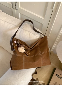 Detail of dark brown tote bag with white stitching and plush bear charm on white sofa