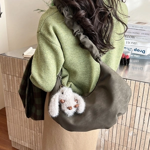 Detail of dark olive hobo bag with ruched strap and plush bunny charm on a model
