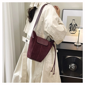 Burgundy matte suede bucket bag shown on shoulder with fringe detail and vertical stitching