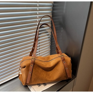 Close-up of brown suede Boston bag with golden adjustable buckle straps and matte texture