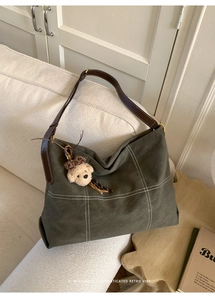 Retro grey-green tote bag with white grid stitching and a plush bear charm on a sofa