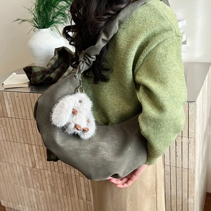 Detail of dark green half-moon hobo bag with pleated strap and rabbit plush pendant