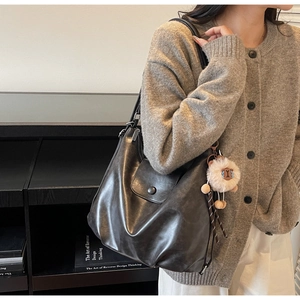 Detail of black leather tote bag featuring a cute beige sheep plush charm decoration