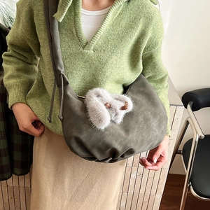 Deep olive green hobo bag with plush bunny charm worn with knitwear and beige skirt