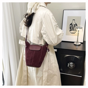 Detail view of burgundy suede bucket bag with side drawstring knot on model shoulder