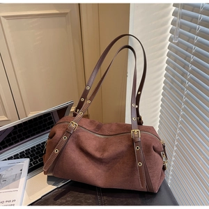 Brown frosted suede Boston shoulder bag with adjustable straps on a leather bench