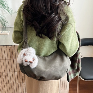 Detail of dark grey-green hobo bag with plush bunny charm on a knitted sweater background