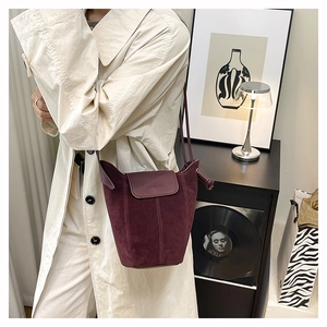 Detailed view of burgundy suede bucket bag styled with a beige trench coat in a home setting