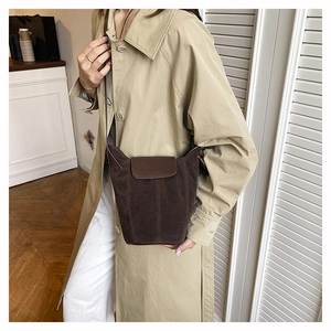 Detail of a dark brown suede bucket bag worn with a khaki trench coat in daily life