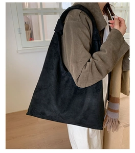 Minimalist black suede tote bag shown on shoulder in a cozy interior setting