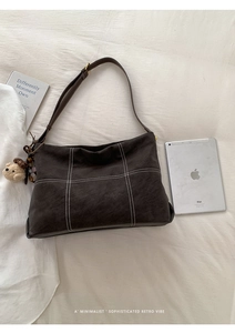 Detail view of coffee brown frosted leather tote bag with white stitching on bed