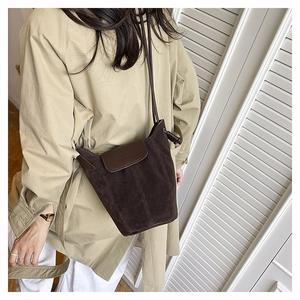 Detail of dark brown suede bucket bag with leather knot strap on a beige trench coat