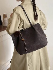 Minimalist large brown tote bag with plush charm shown on a female model shoulder