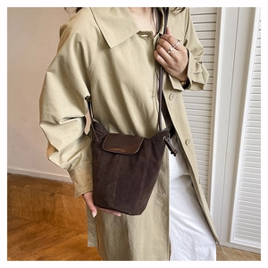 Detail of dark brown suede bucket bag with embossed logo and minimalist flap design
