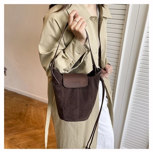 Close-up of dark brown suede bucket bag with adjustable strap and MANI JIA brand embossing