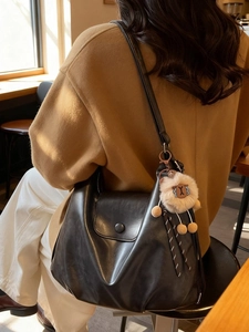 Black leather hobo shoulder bag with plush charm shown in a minimalist cafe setting