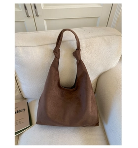 Detail shot of a dark brown suede tote bag with a unique knotted handle on a soft sofa