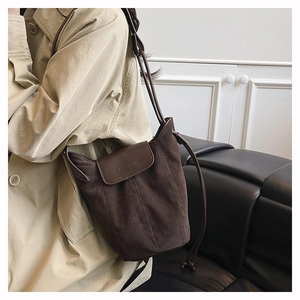 Detail of dark brown suede bucket bag with leather flap and drawstring closure