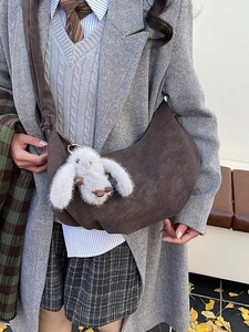 Brown suede crescent shoulder bag with plush rabbit pendant in minimalist casual style