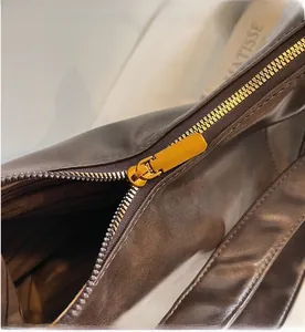Detailed close-up of smooth gold metal zipper on soft brown leather tote bag