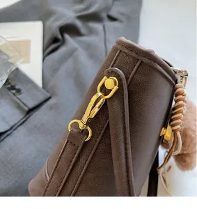 Detailed shot of dark brown pebbled leather bag featuring a gold clasp and plush charm