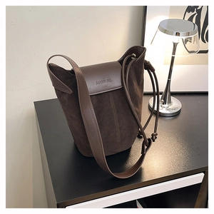 Detailed close-up of dark brown suede bucket bag with leather flap and brand embossing