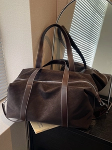 Large dark brown suede travel tote bag with leather straps shown in a home setting