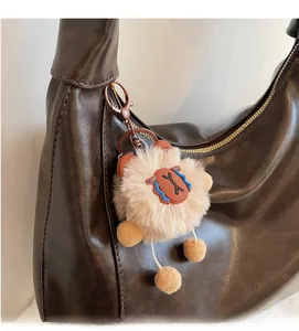 Detail of soft plush teddy bear charm attached to a brown leather tote bag