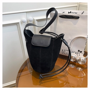 Close-up of black matte suede bucket bag featuring smooth leather flap and embossed logo