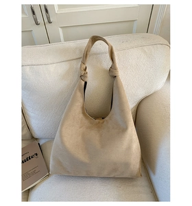 Minimalist beige suede tote bag with decorative knots on a white fabric sofa