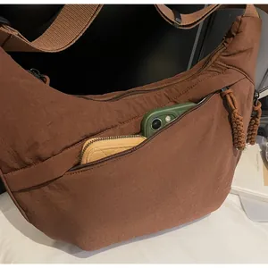 Detail of a brown nylon crossbody bag showing the front zipper pocket with phone storage