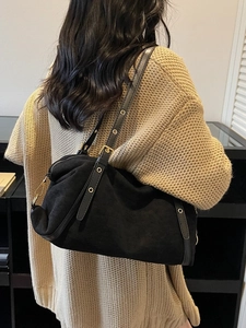 Minimalist black matte shoulder bag with gold hardware worn over a beige knit sweater