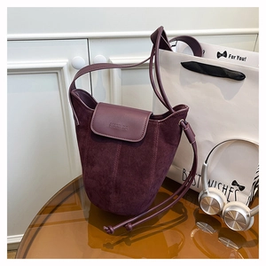 Macro view of burgundy suede bucket bag featuring high-quality leather stitching and logo