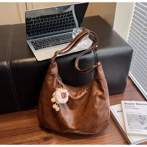 Detail of a large brown faux leather hobo tote bag with a white plush sheep charm
