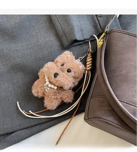 Close-up of a brown plush dog keychain with pearl necklace on a leather bucket bag