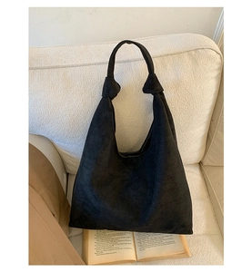 Detail of black suede hobo bag with knot strap on white fabric background