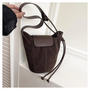Detailed macro view of dark brown suede bucket bag featuring embossed leather logo flap
