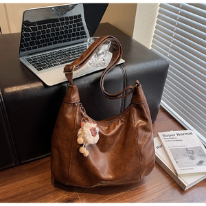 Brown soft leather hobo bag on wooden floor with plush charm and office accessories