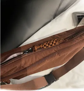 Detail of smooth metal zipper and woven strap on brown nylon crossbody bag